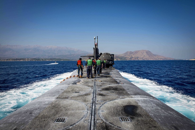 Sailors stand on top of a submarine as it travels through waters.