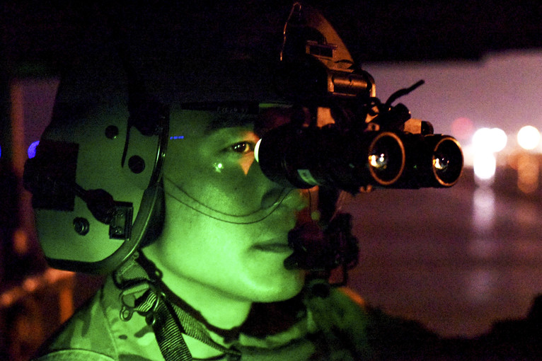 An airman, illuminated in green light, looks through lenses attached to his helmet.